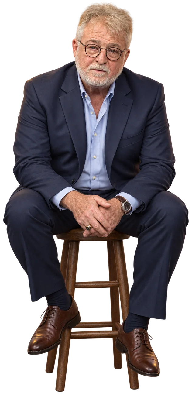 Greg Langford seated on a wooden stool, leaning forward to tell a story